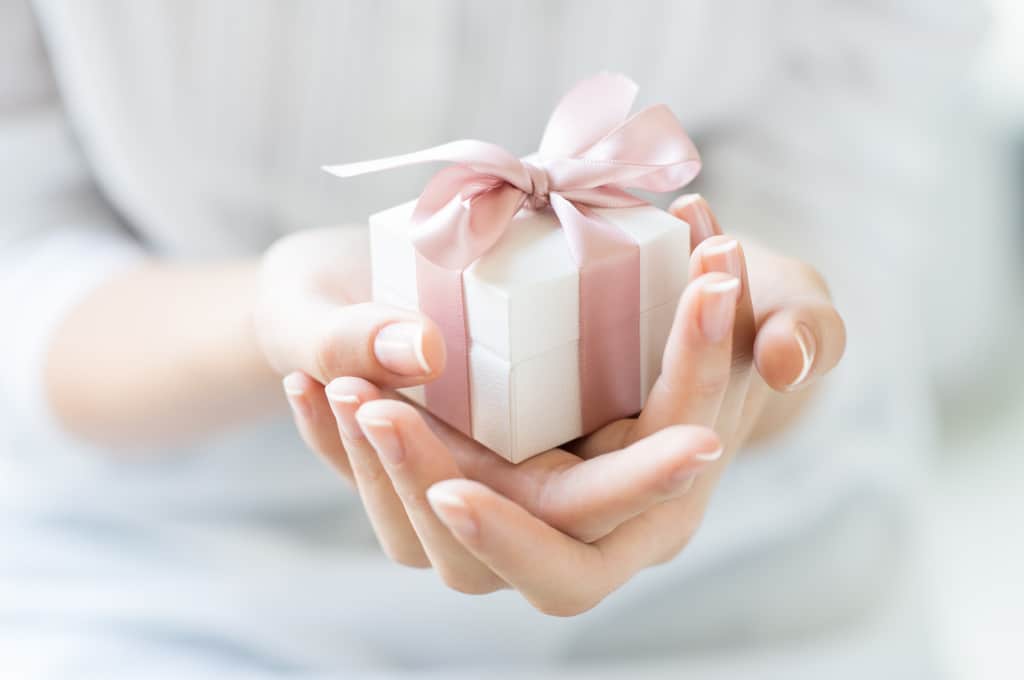Hands gently cradle a small white gift box adorned with a pink ribbon, perfect as a thoughtful Christmas gift for your nanny.