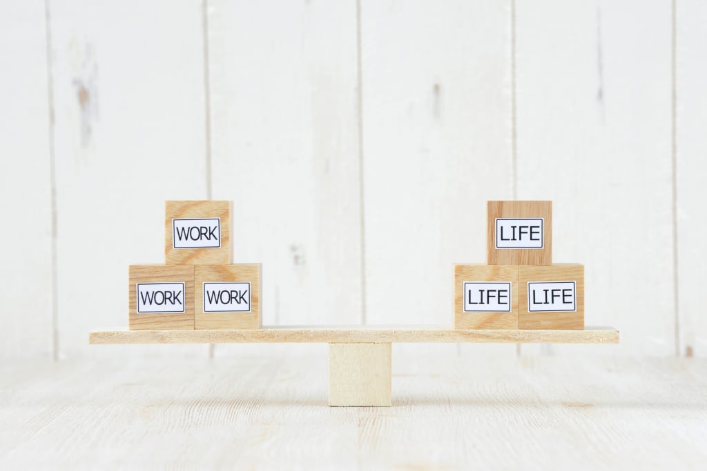 Balanced wooden blocks labeled "WORK" and "LIFE" on a seesaw, illustrating work-life balance akin to navigating the fifth trimester.