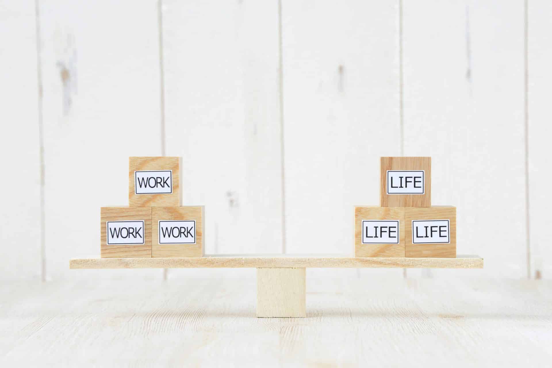 Balanced wooden blocks labeled "WORK" and "LIFE" on a seesaw, illustrating work-life balance akin to navigating the fifth trimester.