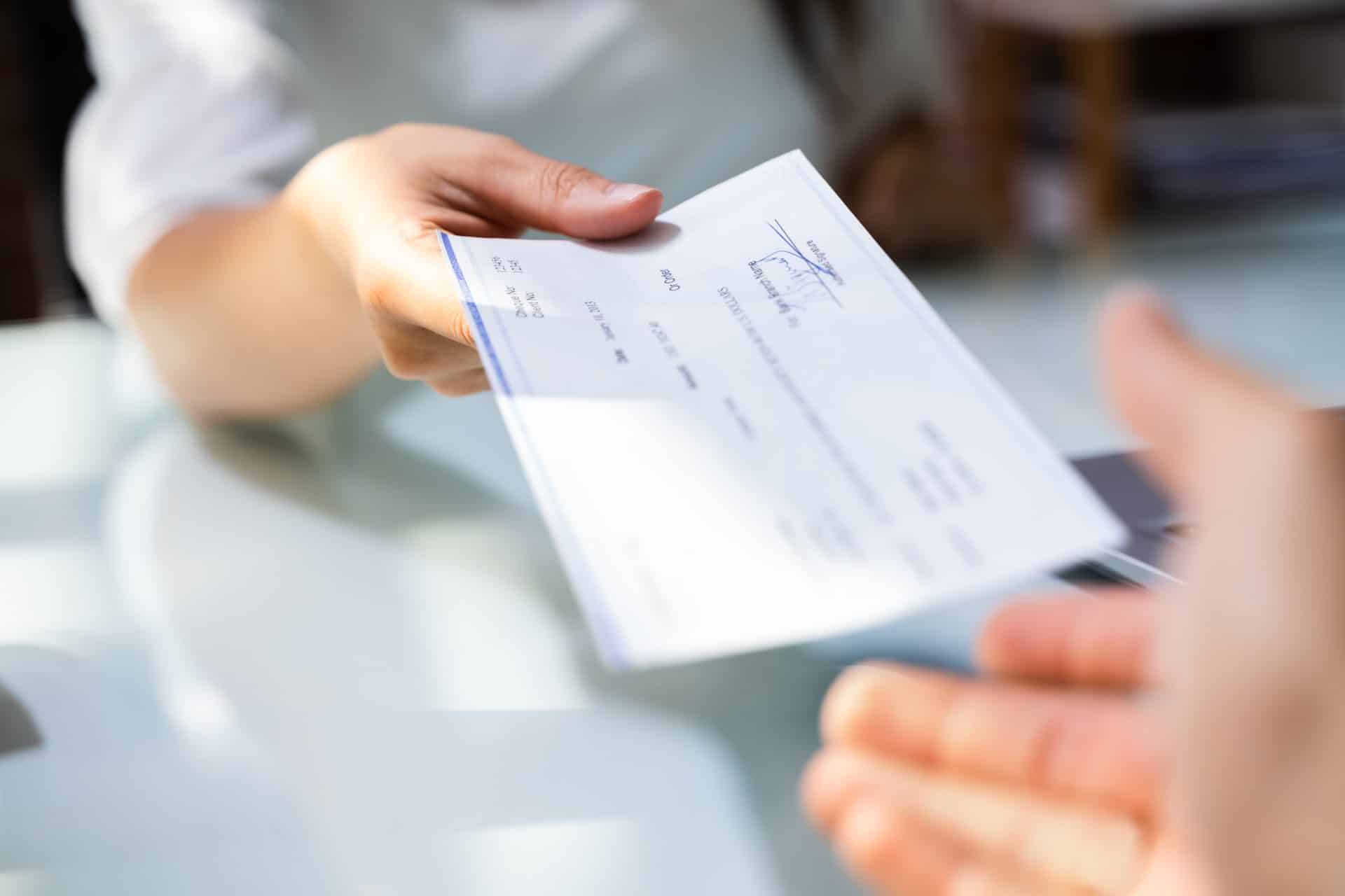 In an office setting, a person is handing over a check for the legal nanny payroll to another across the desk.