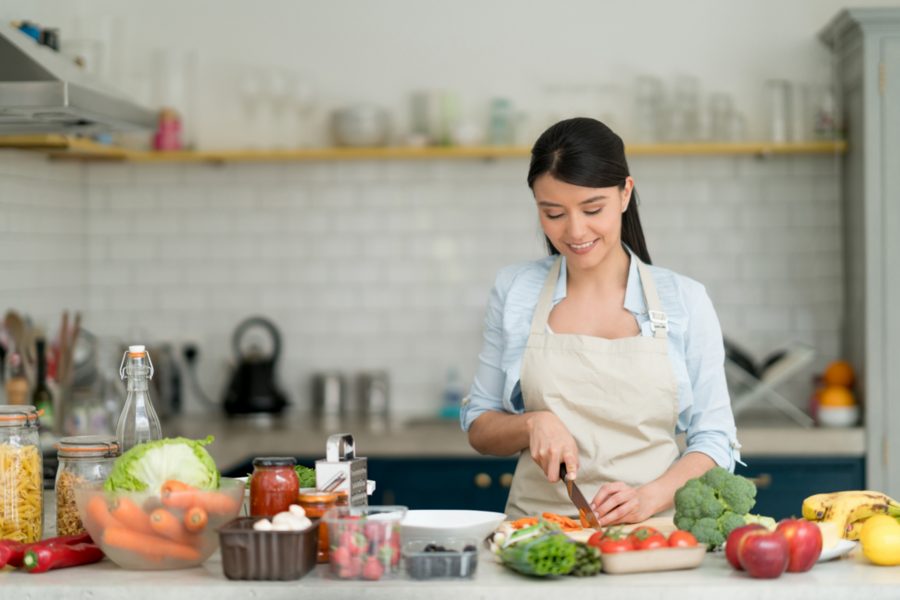In a bright kitchen, a woman in an apron chops vegetables, mirroring the care and dedication of a live-in nanny.