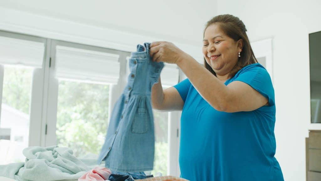 A woman, possibly a live-in nanny, smiles warmly as she folds clothes by the window, basking in the gentle embrace of natural light.