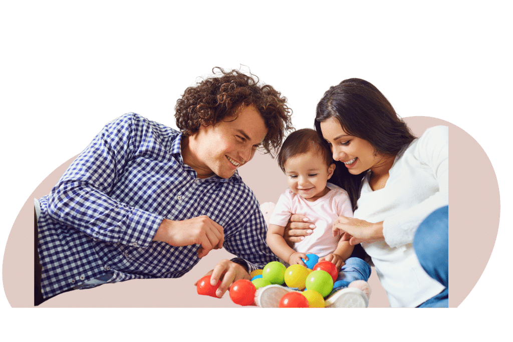 A family with a young child plays with colorful balls while lying on the floor, smiling and enjoying their time together.
