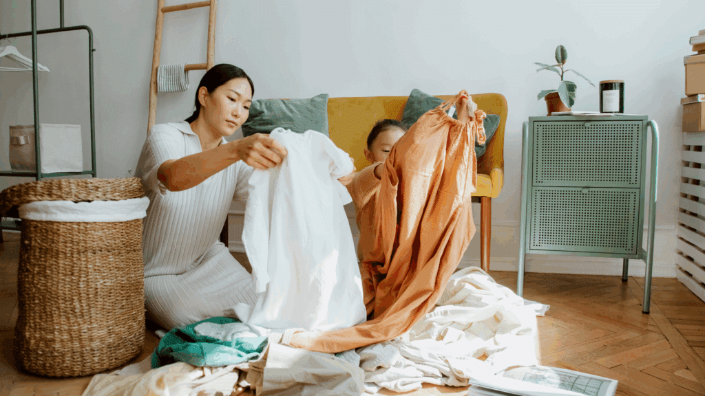 A woman and a child sit on the floor, folding laundry in a bright, cozy living room, showcasing how family assistants can support daily household routines.