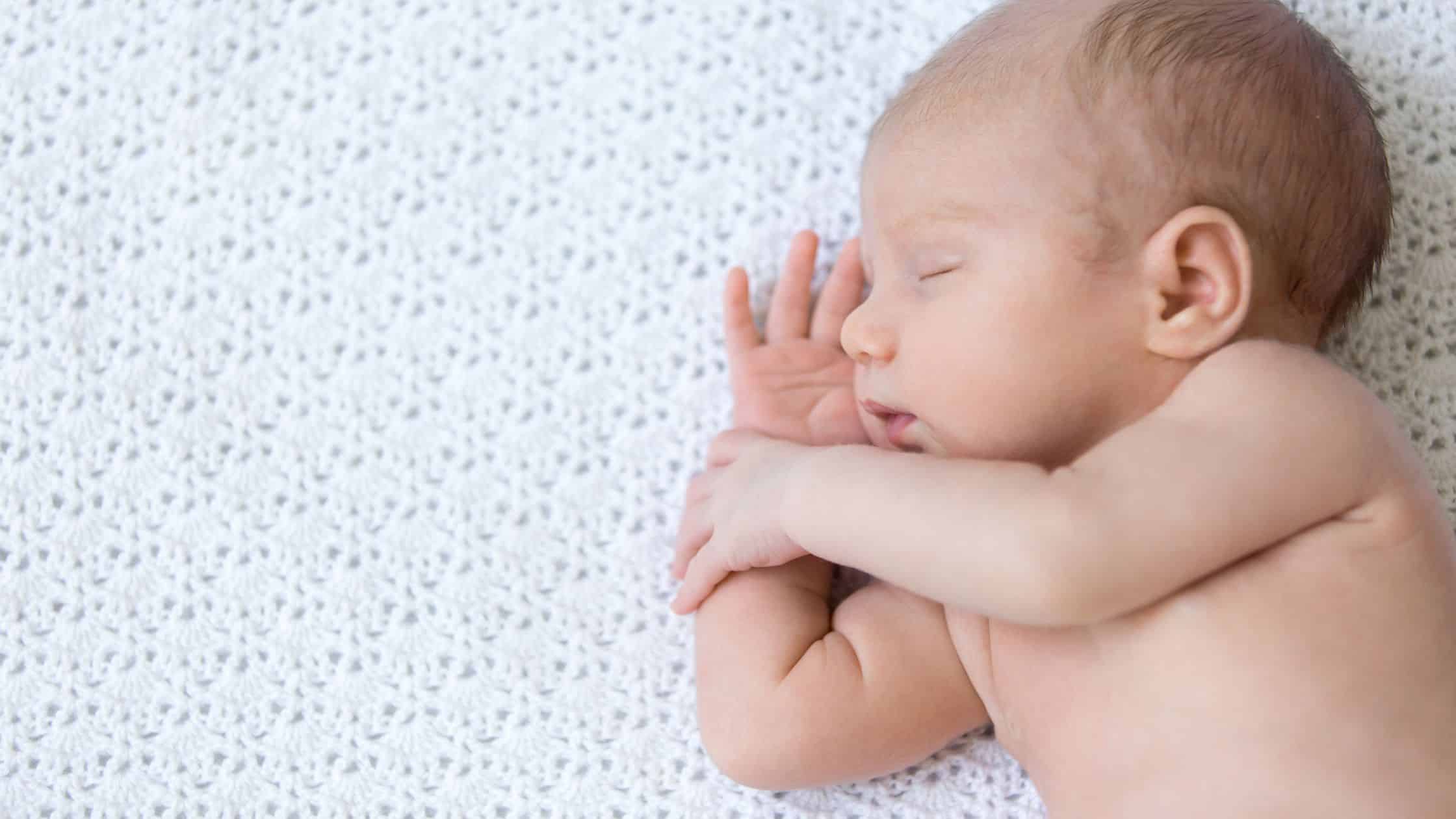 Newborn baby sleeping peacefully on a soft white blanket, capturing a serene moment that inspires many to learn how to become a newborn care specialist.