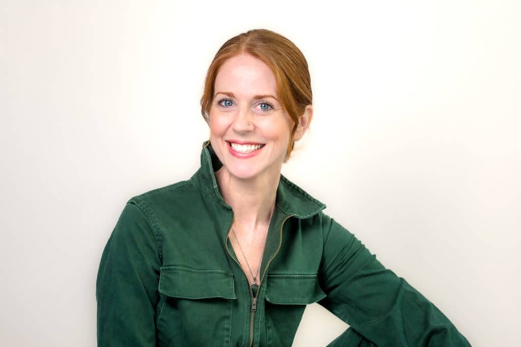 Smiling woman with red hair in a green jacket poses against a plain light background, reminiscent of the style seen in the Keesha Scott interview.
