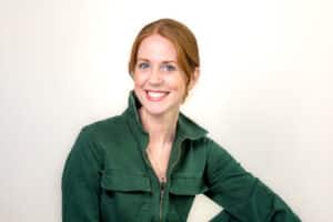 Smiling woman with red hair in a green jacket poses against a plain light background, reminiscent of the style seen in the Keesha Scott interview.