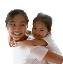 Smiling woman giving a piggyback ride to a happy young girl, both wearing white shirts.